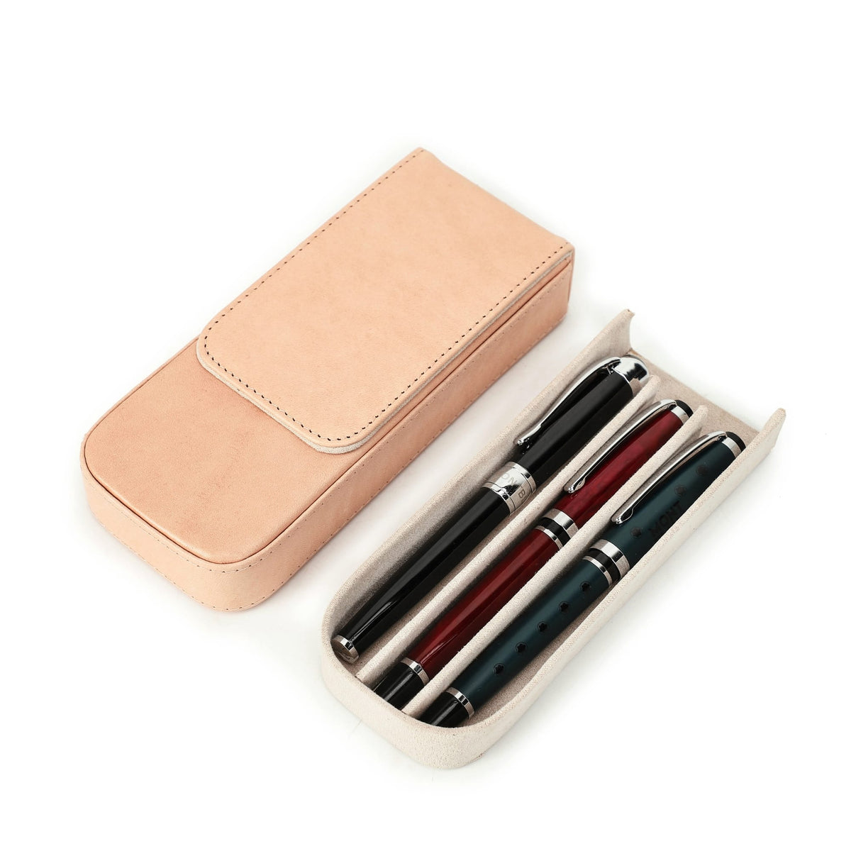 Leather three-pen case resting on a desk beside writing tools